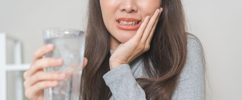 Woman with sensitive teeth, holding glass of ice water
